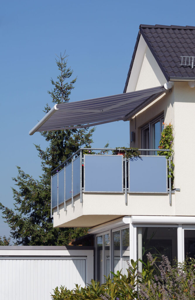 Moderner Balkon mit ausgefahrener Markise an einem Einfamilienhaus bei sonnigem Wetter.