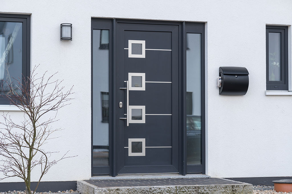 Moderne Haustür mit geometrischem Design und Glaselementen an einem weißen Wohnhaus.